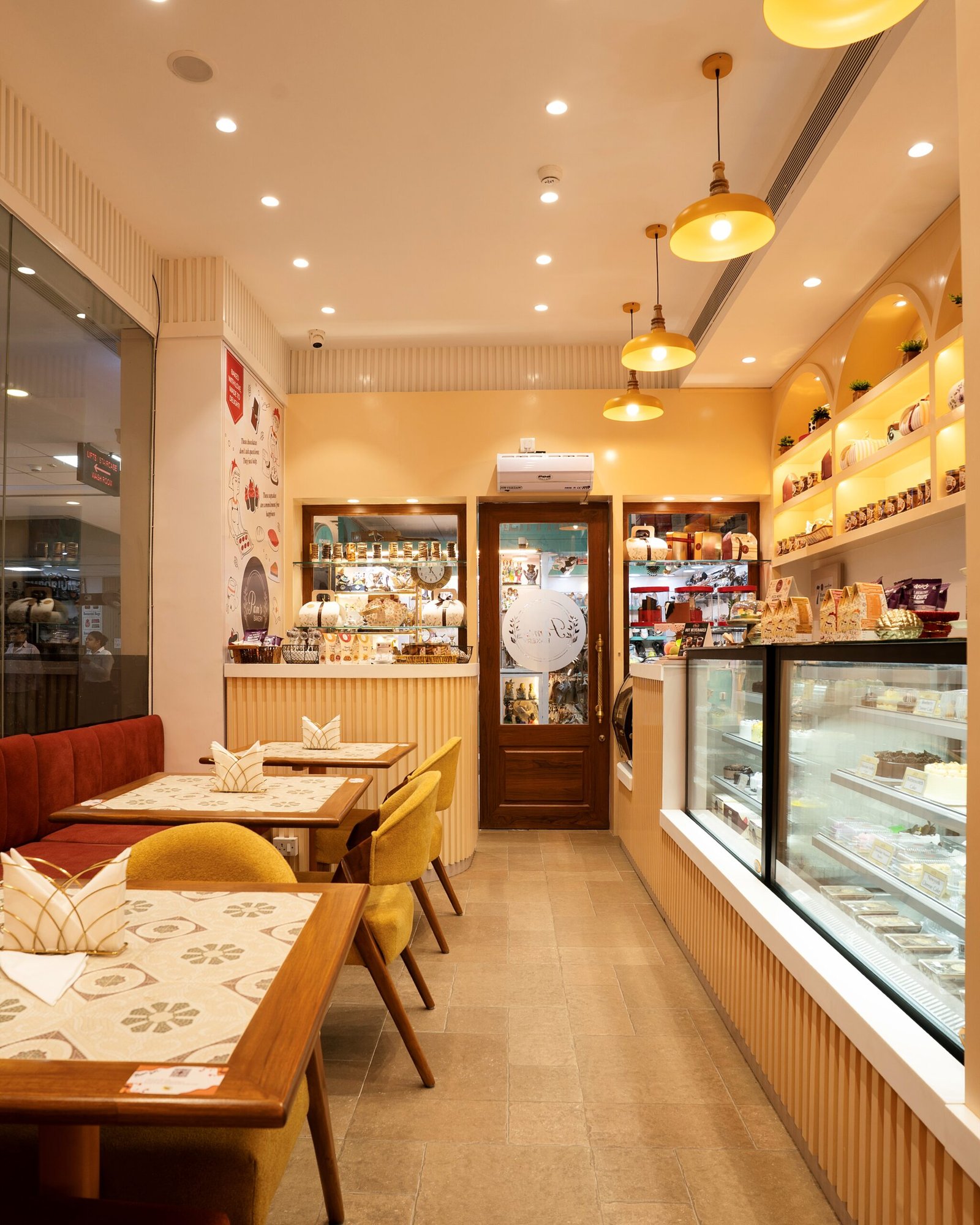 Pam’s Bakery café interior with dining tables, dessert display cases, product shelves, and warm lighting