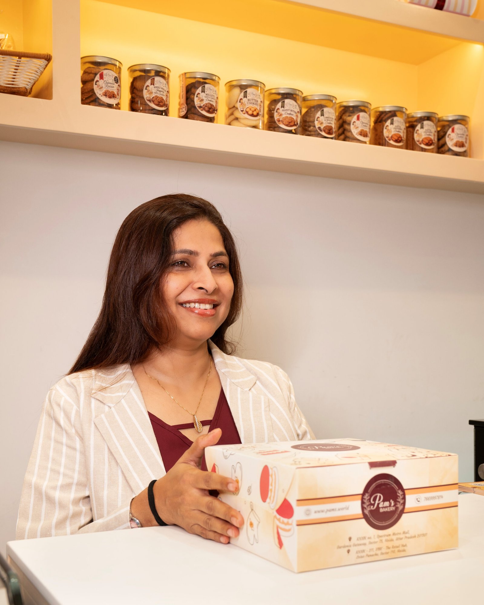 Smiling woman holding a Pam's Bakery packaged gift box in the bakery