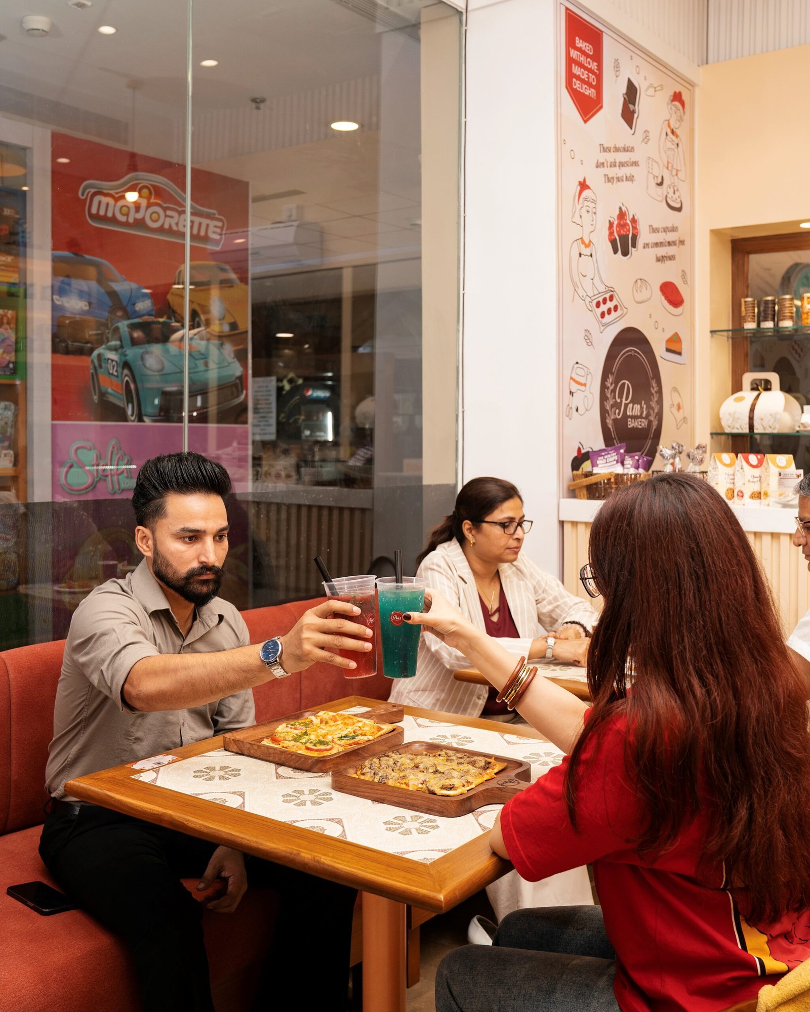Three customers enjoying food and raising their branded beverages together at Pam’s Bakery café.